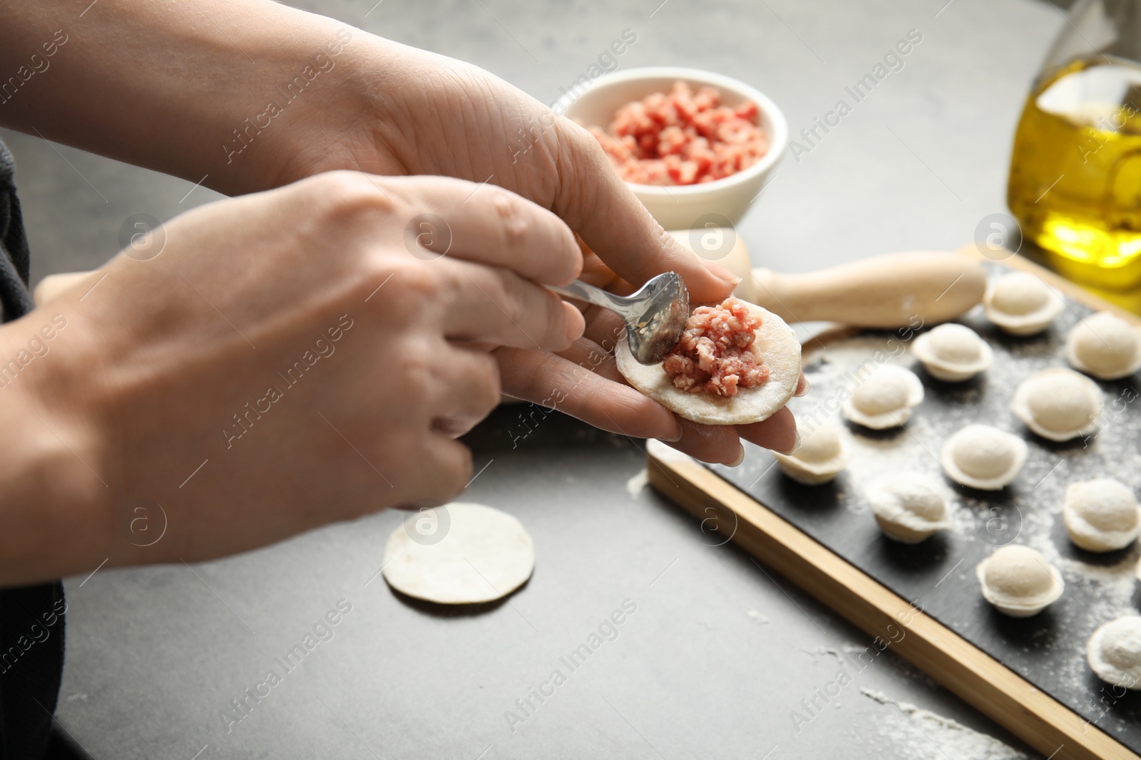 Photo of Woman cooking delicious dumplings over grey table, closeup