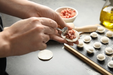 Photo of Woman cooking delicious dumplings over grey table, closeup