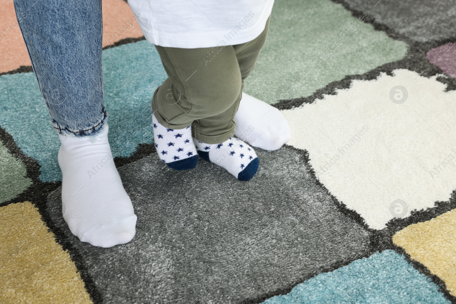 Photo of Mother supporting her son while he learning to walk on carpet, closeup. Space for text