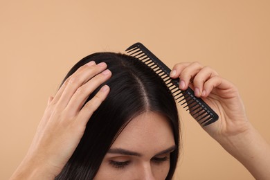 Woman with comb examining her hair and scalp on beige background, closeup