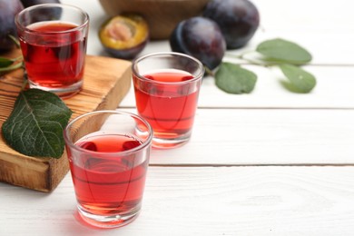 Photo of Delicious plum liquor and ripe fruits on white wooden table, space for text. Homemade strong alcoholic beverage