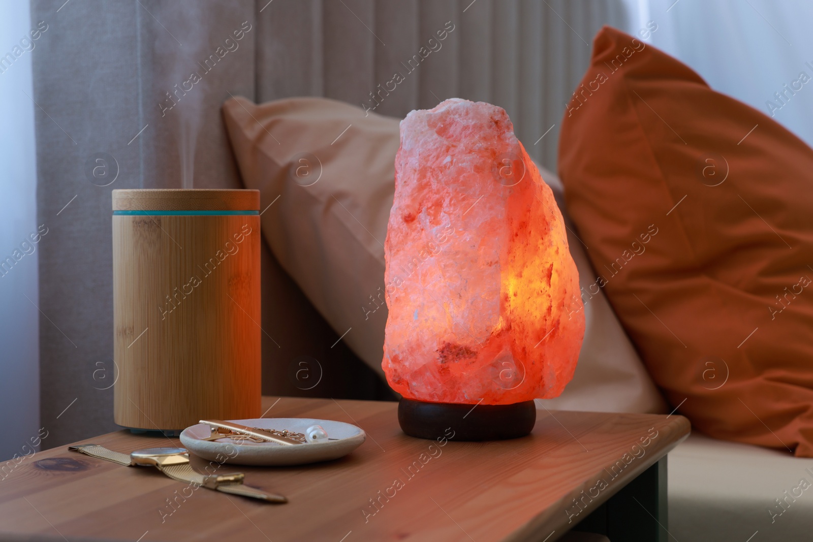 Photo of Himalayan salt lamp, air ionizer and accessories on nightstand in bedroom