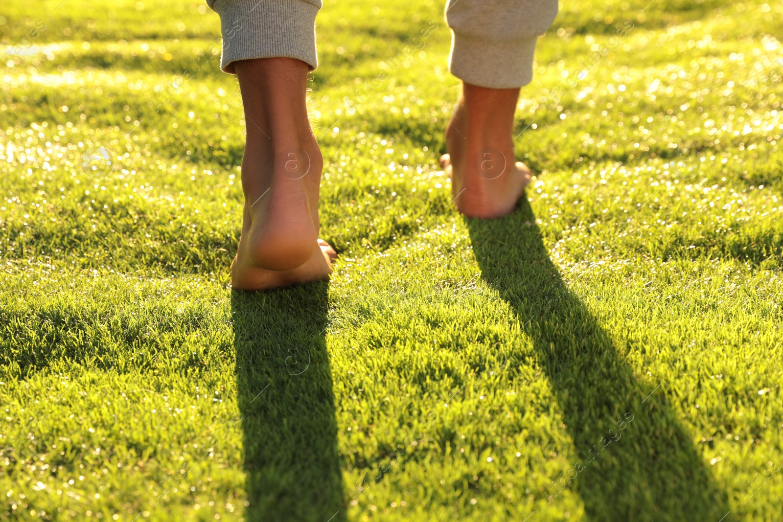 Photo of Man walking barefoot on fresh green grass, closeup