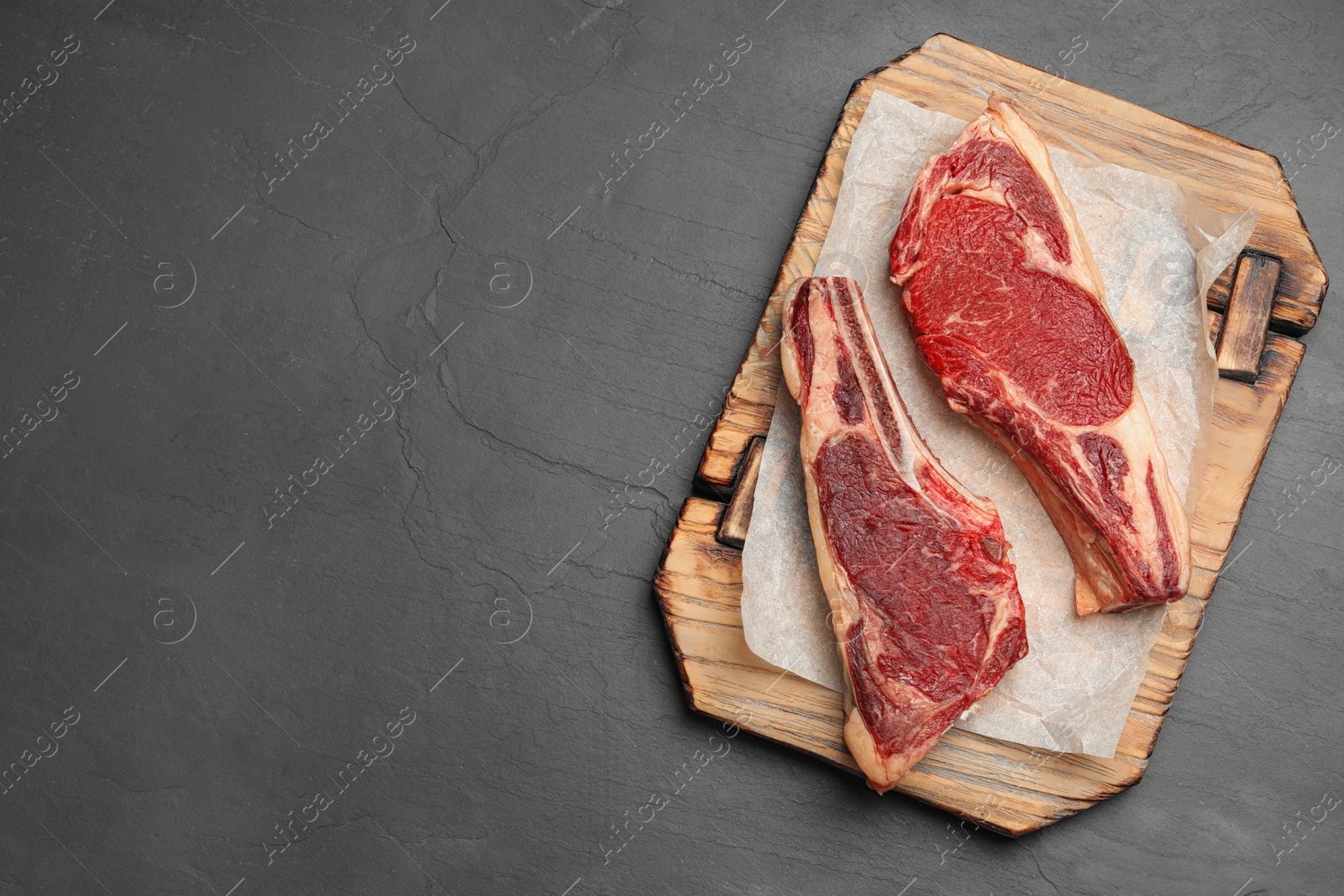 Photo of Wooden board with raw beef meat on black table, flat lay. Space for text