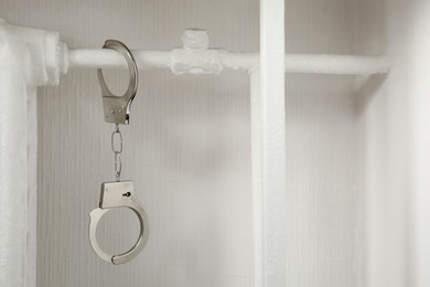 Photo of Handcuffs hanging on radiator near white wall indoors