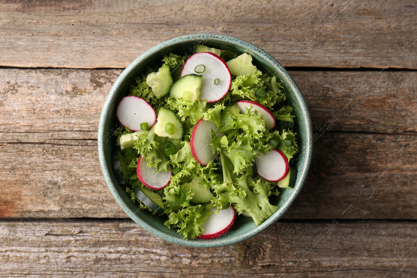 Photo of Delicious salad with radish, lettuce and cucumbers in bowl on wooden table, top view