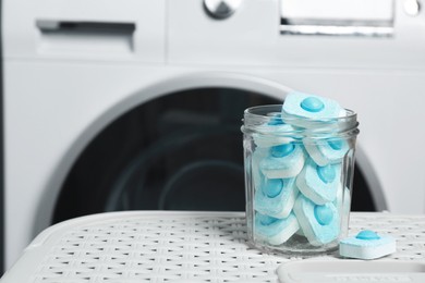 Jar with water softener tablets on laundry basket near washing machine