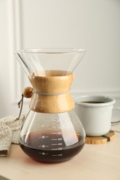 Photo of Glass chemex coffeemaker with coffee and cup on table, closeup