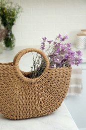 Photo of Stylish beach bag with beautiful bouquet of wildflowers on white table in kitchen