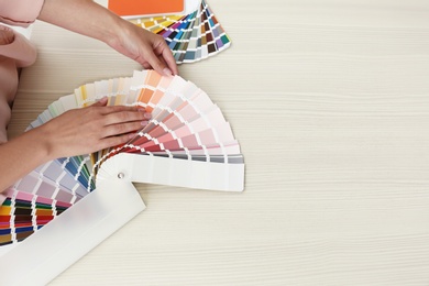 Photo of Female interior designer with color palette samples at wooden table, closeup. Space for text
