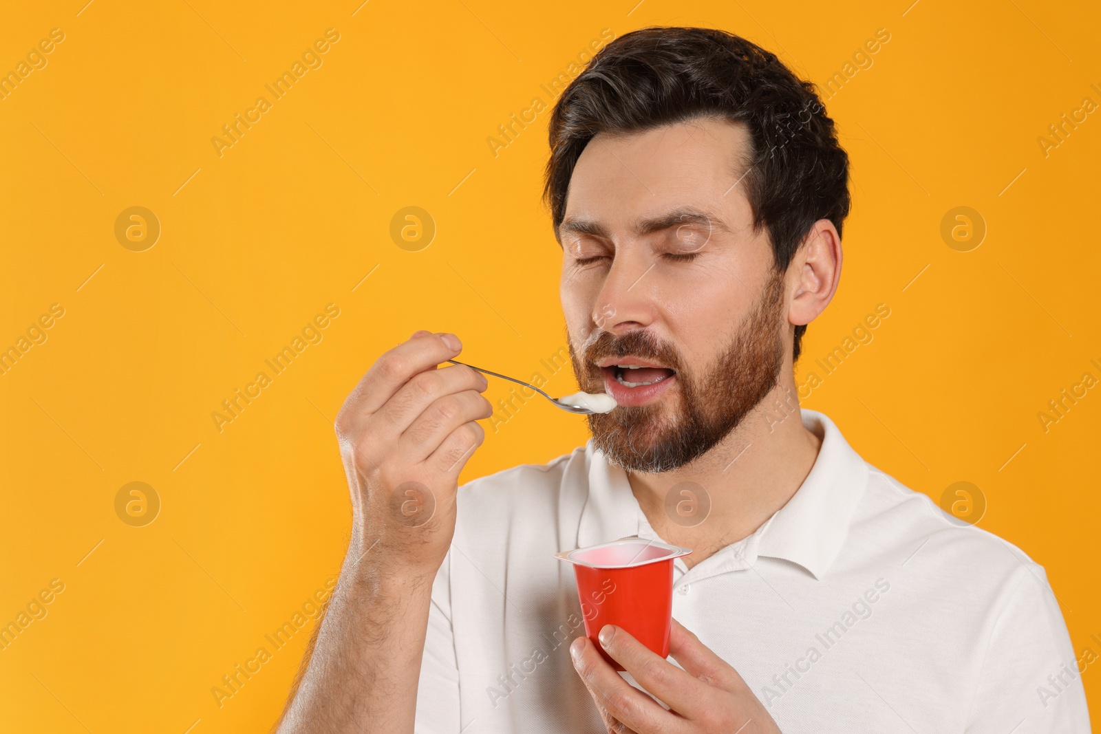 Photo of Handsome man eating delicious yogurt on yellow background. Space for text