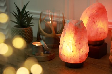 Himalayan salt lamps, candles, houseplant and gemstones on wooden table near white wall indoors. Bokeh effect