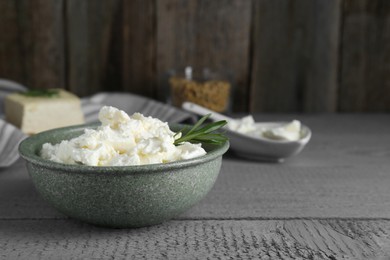 Photo of Delicious tofu cream cheese with rosemary in bowl on grey wooden table, space for text