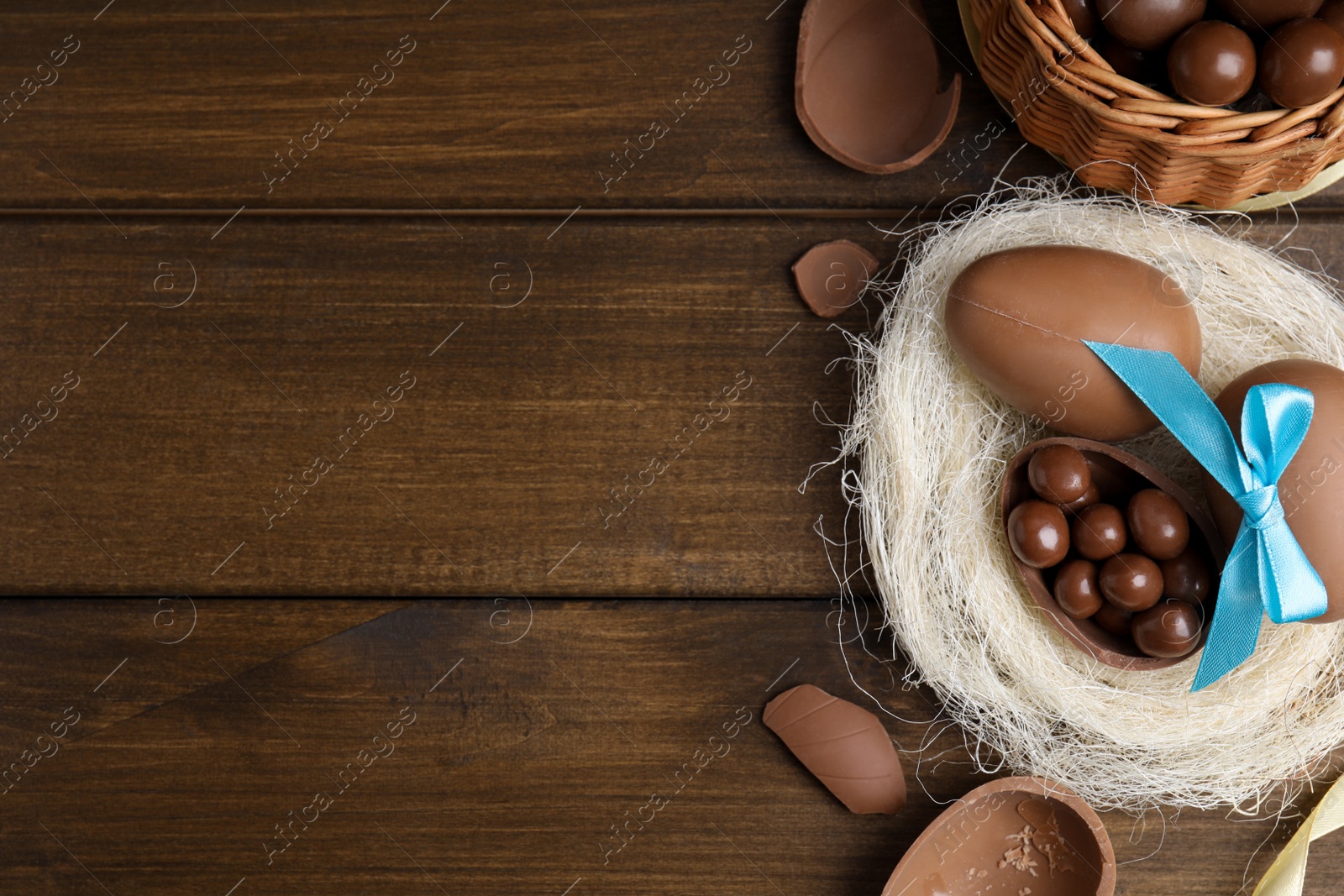 Photo of Tasty chocolate eggs with candies in decorative nest on wooden table, flat lay. Space for text