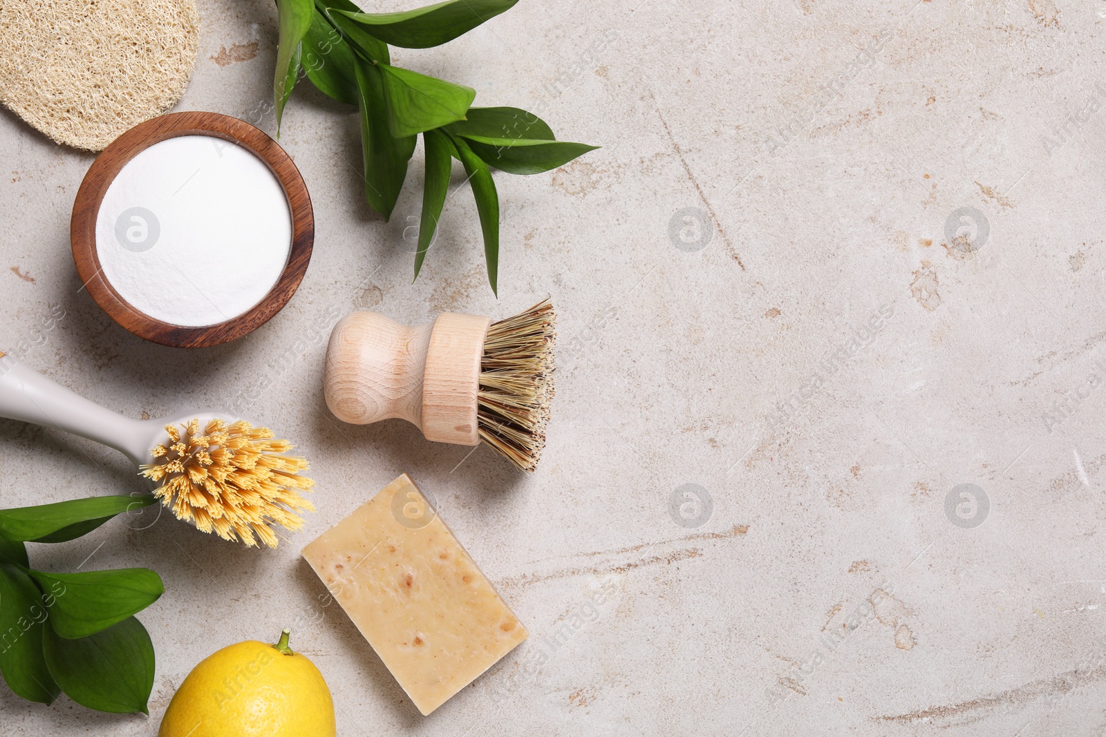 Photo of Cleaning brushes, baking soda, lemon, soap and green leaves on light grey table, flat lay. Space for text