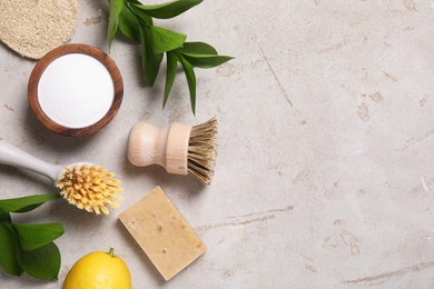 Photo of Cleaning brushes, baking soda, lemon, soap and green leaves on light grey table, flat lay. Space for text