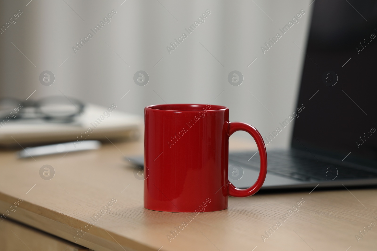 Photo of Red ceramic mug and laptop on wooden table at workplace