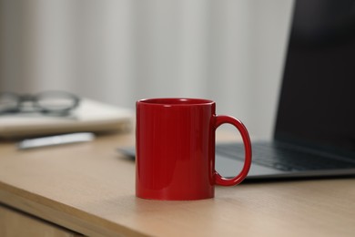 Photo of Red ceramic mug and laptop on wooden table at workplace