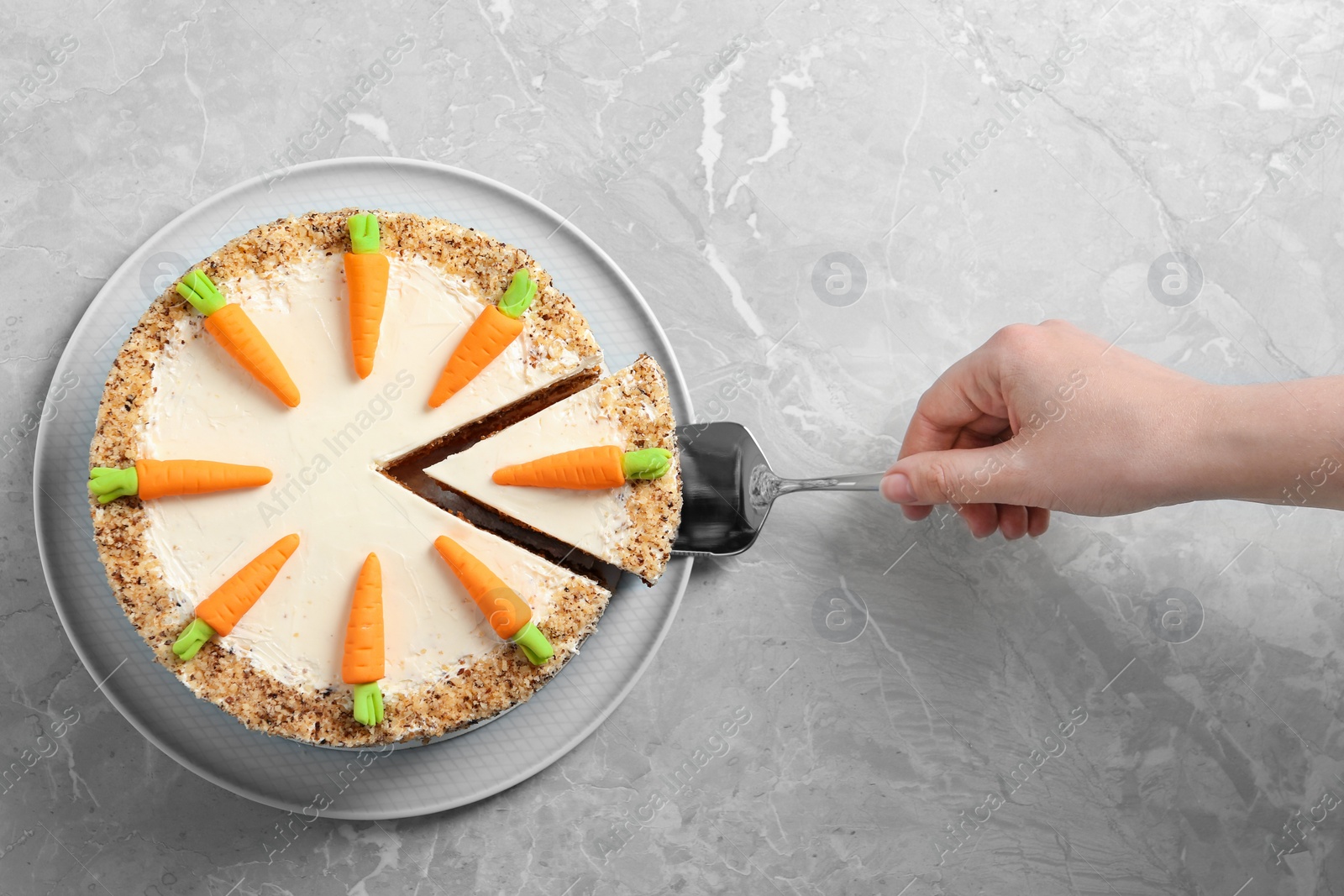 Photo of Woman taking piece of sweet carrot cake with delicious cream at grey marble table, top view