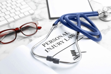 Book with words PERSONAL INJURY LAW and stethoscope on table, closeup