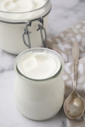 Delicious natural yogurt in glass jars and spoon on white marble table, closeup