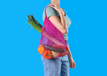 Photo of Woman holding net bag with vegetables on light blue background, closeup