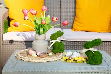 Photo of Terrace with Easter decorations. Bouquet of tulips in vase, bunny figures and decorated eggs on table outdoors