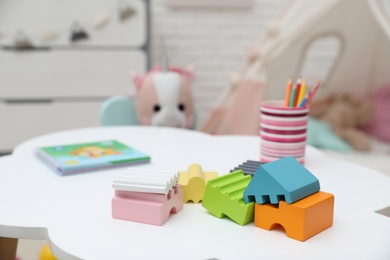 Photo of Bright toys, pencils and book on white table in playroom
