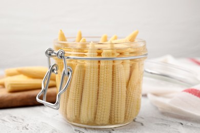 Jar of pickled baby corn on white textured table, closeup