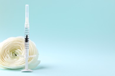 Photo of Cosmetology. Medical syringe and ranunculus flower on light blue background, space for text