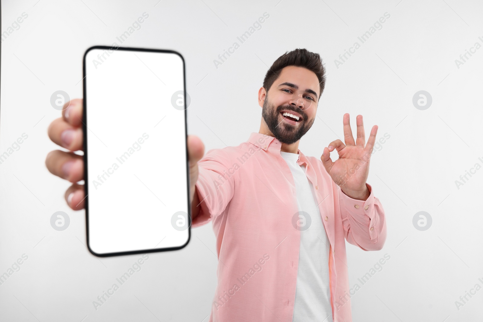 Photo of Young man showing smartphone in hand and OK gesture on white background