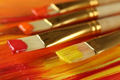 Photo of Set of different brushes on abstract colorful paint, closeup