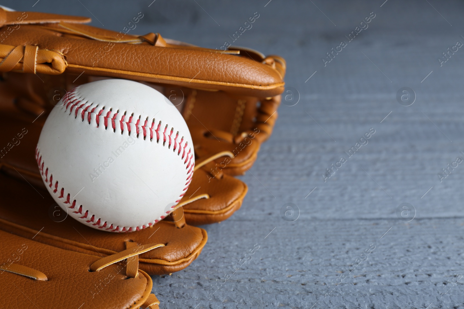 Photo of Leather baseball glove with ball on grey wooden table, closeup. Space for text