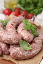 Raw homemade sausages, basil leaves and peppercorns on table, closeup
