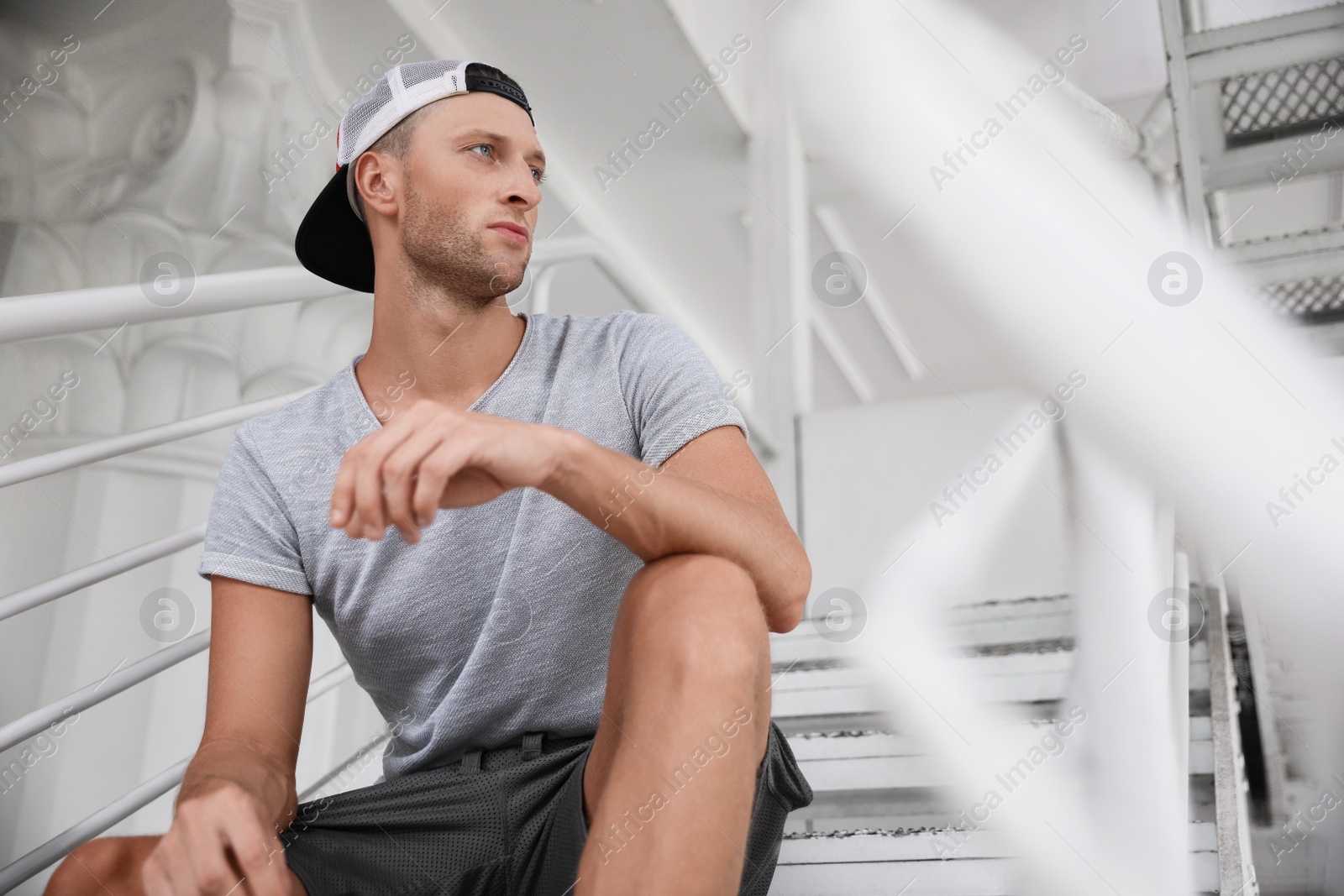 Photo of Handsome young man in stylish cap sitting on stairs, space for text