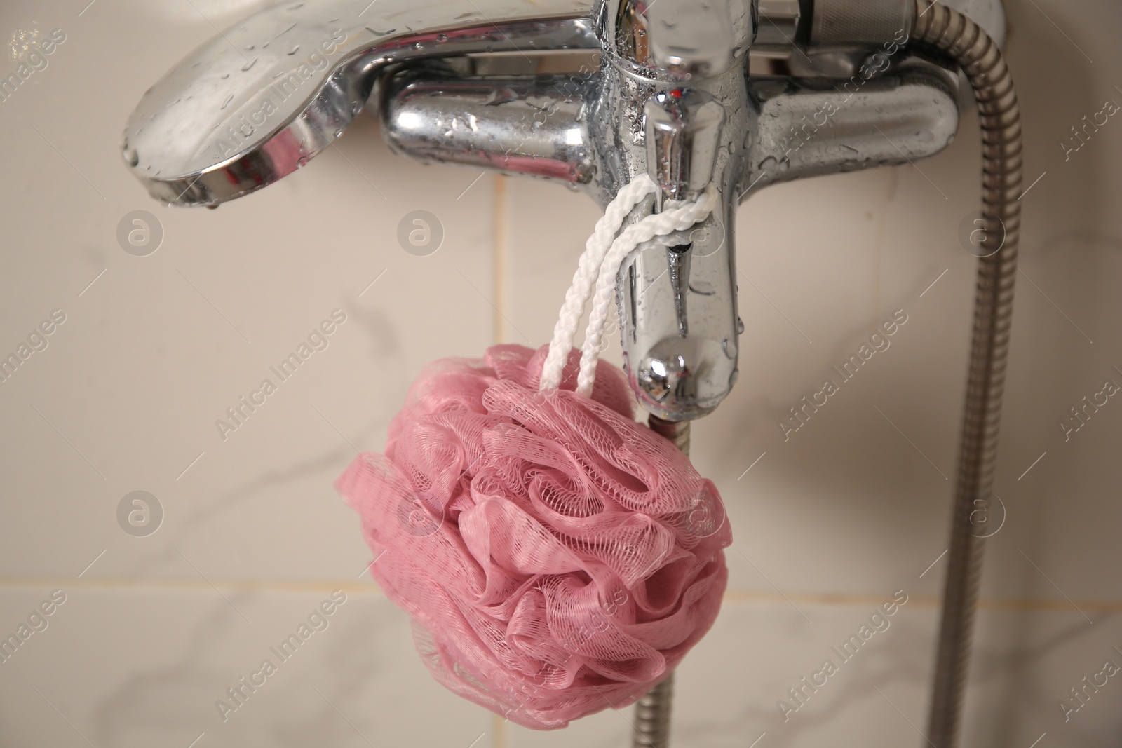 Photo of Pink shower puff hanging on faucet in bathroom, closeup