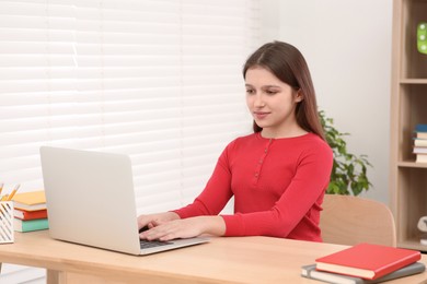 Cute girl using laptop at desk in room. Home workplace