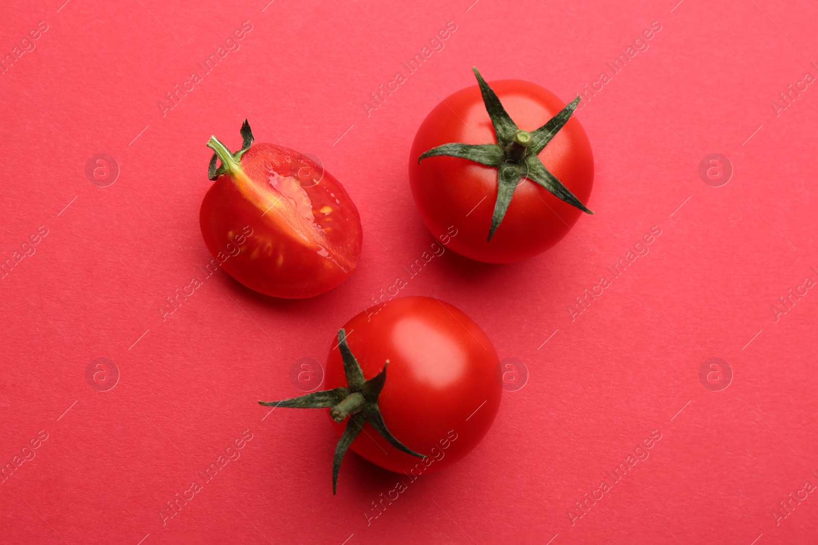 Photo of Whole and cut fresh cherry tomatoes on red background, flat lay