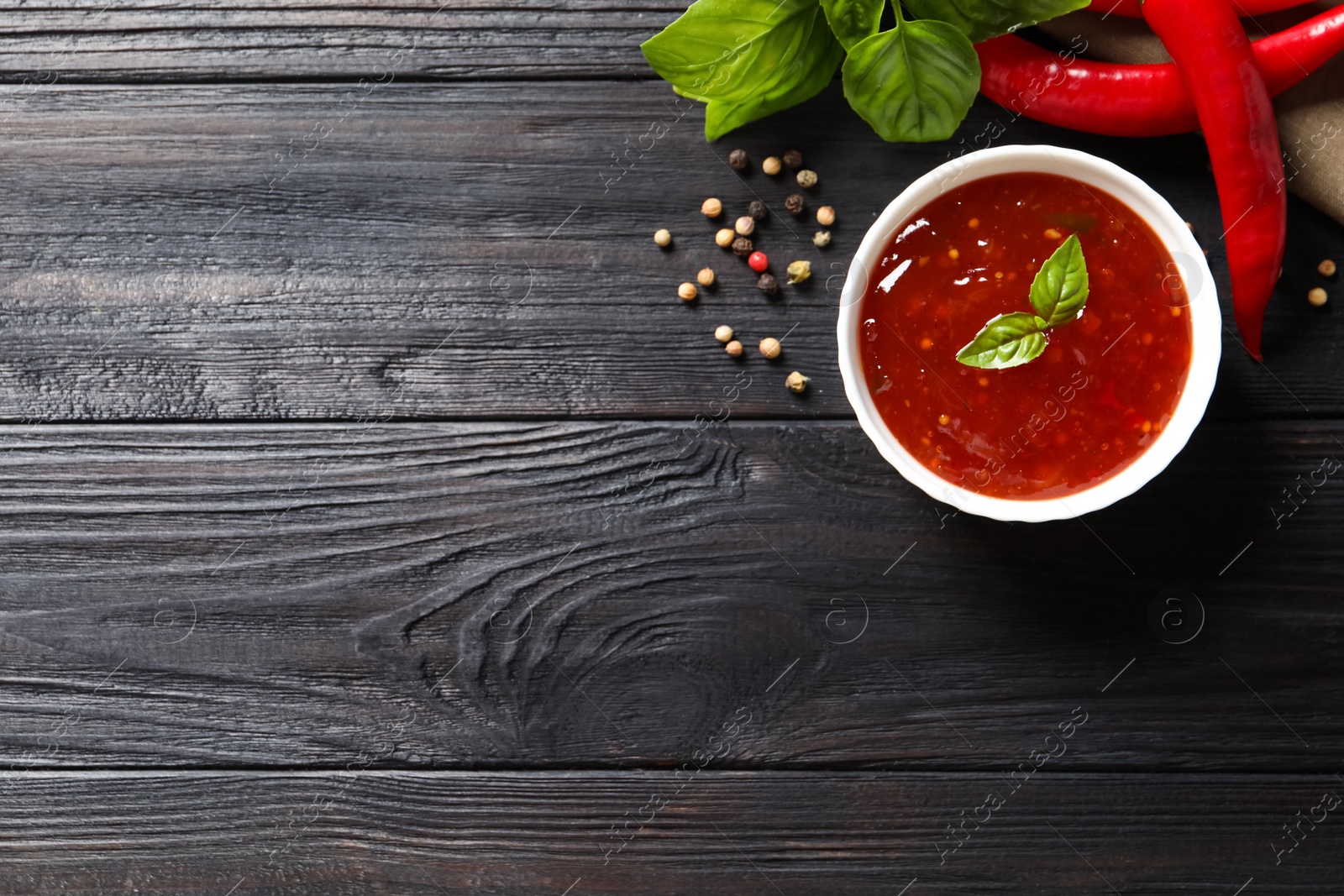 Photo of Spicy chili sauce and ingredients on dark wooden table, flat lay. Space for text