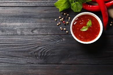 Photo of Spicy chili sauce and ingredients on dark wooden table, flat lay. Space for text