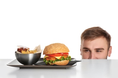 Young man and plate with French fries and tasty burger on white background