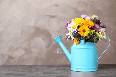 Watering can with beautiful wild flowers on table against grey background