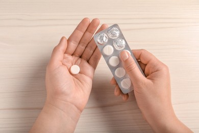 Photo of Woman holding pill and blister at white wooden table, closeup