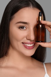 Photo of Beautiful young woman with essential oil on light grey background, closeup