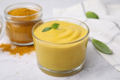 Photo of Tasty curry sauce, powder and basil leaves on white table, closeup