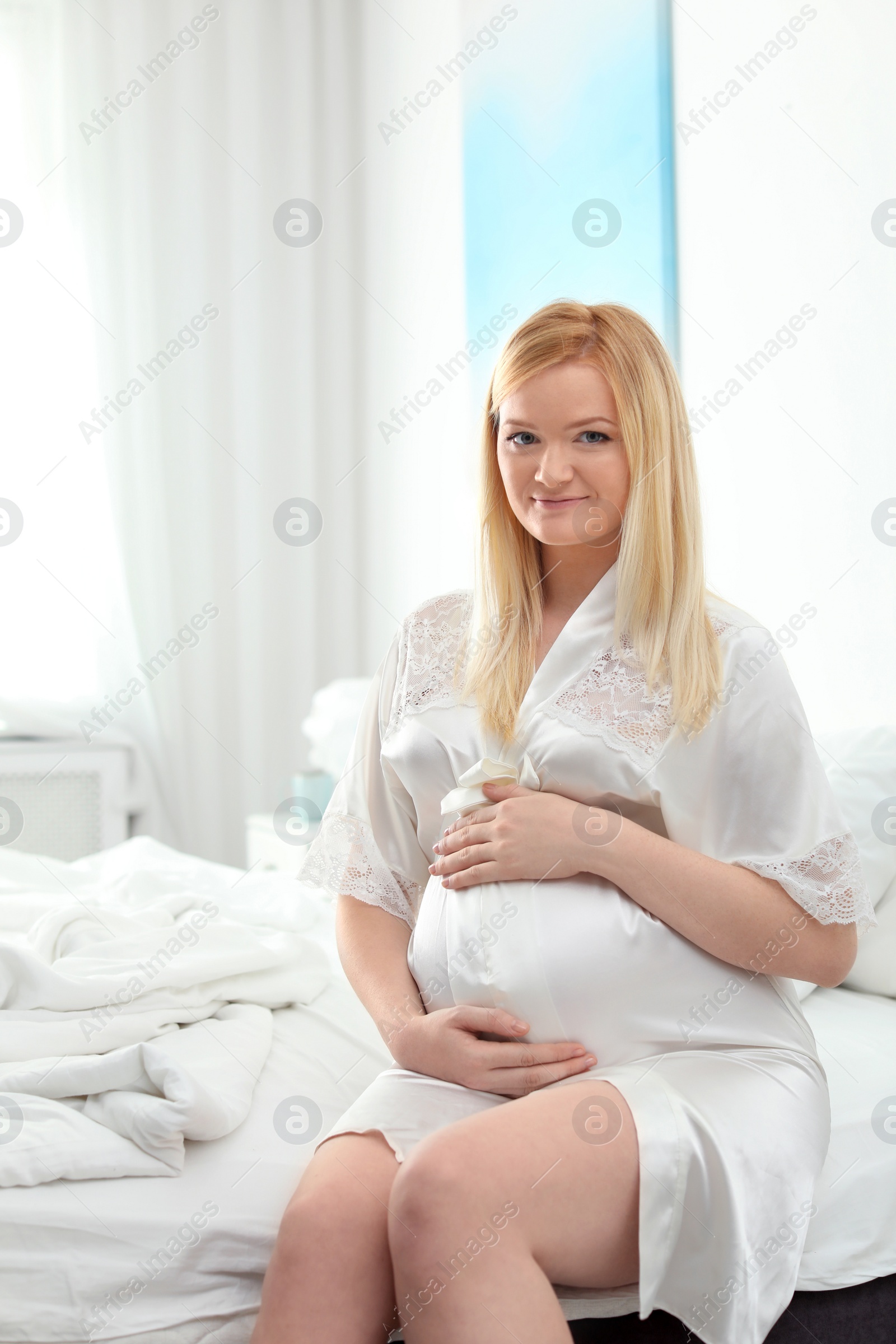 Photo of Beautiful pregnant woman sitting on bed in light room