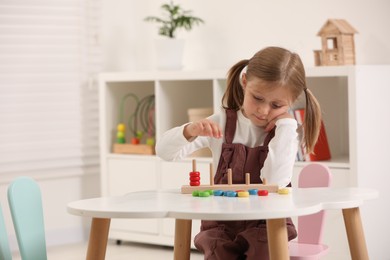 Photo of Cute little girl playing with stacking and counting game at white table indoors, space for text. Child's toy