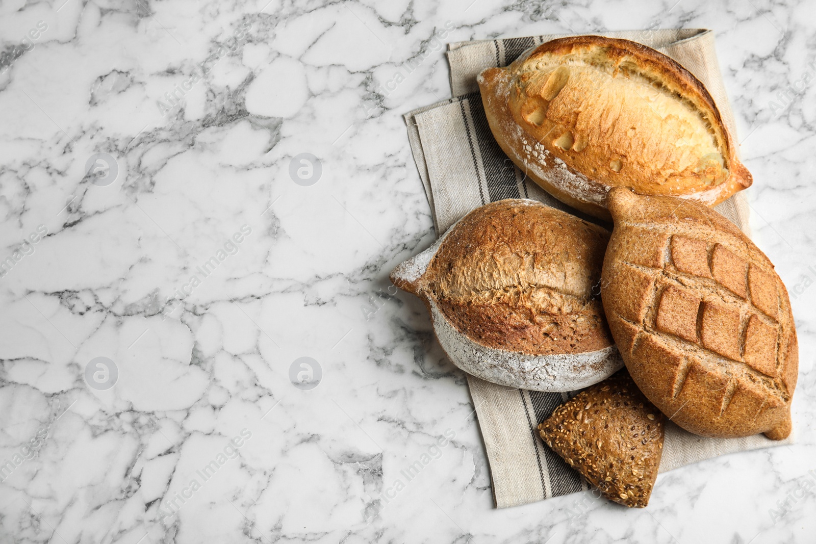 Photo of Different kinds of fresh bread on marble table, top view with space for text