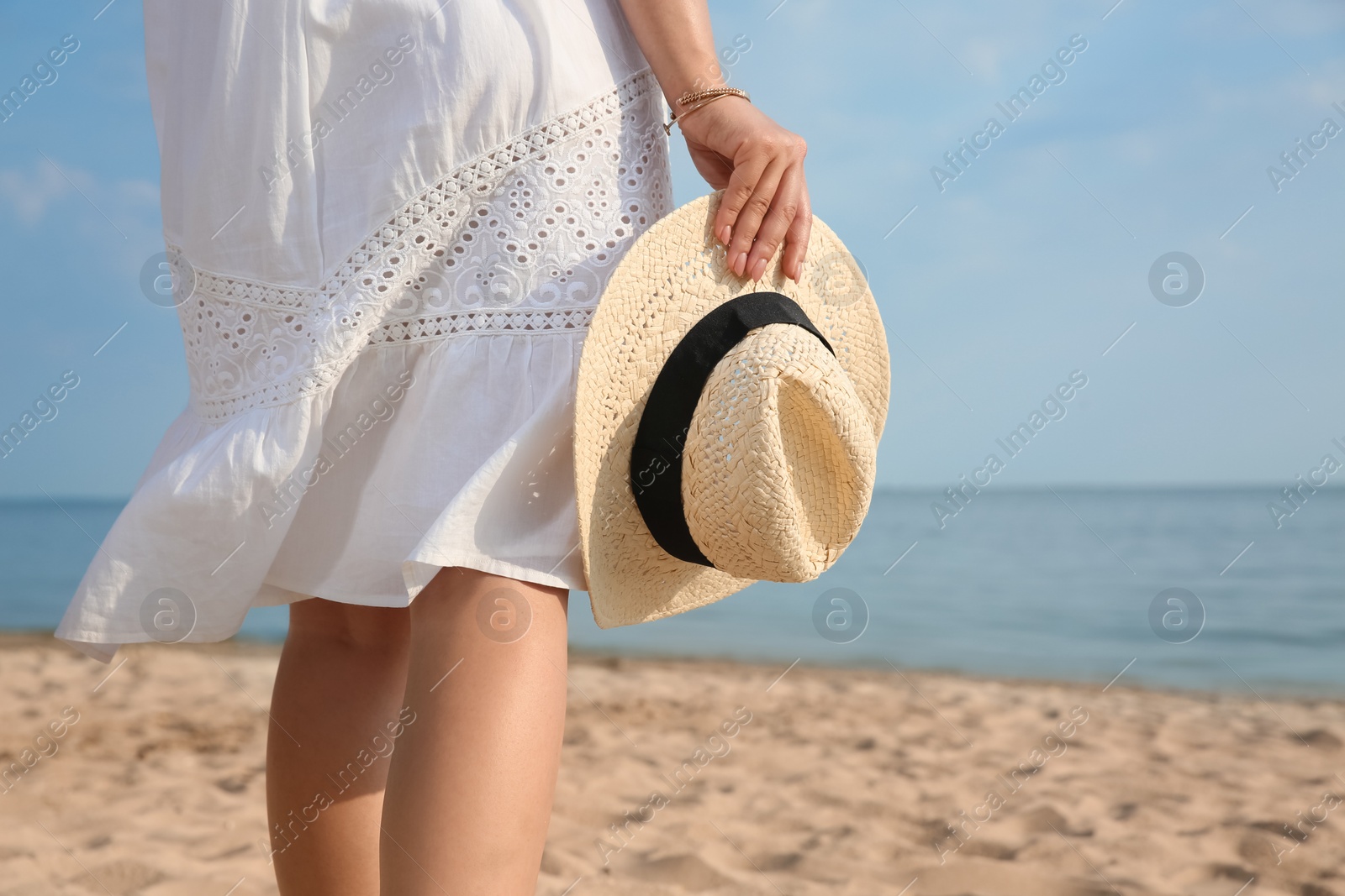 Photo of Beautiful young woman with straw hat on beach, closeup. Stylish headdress