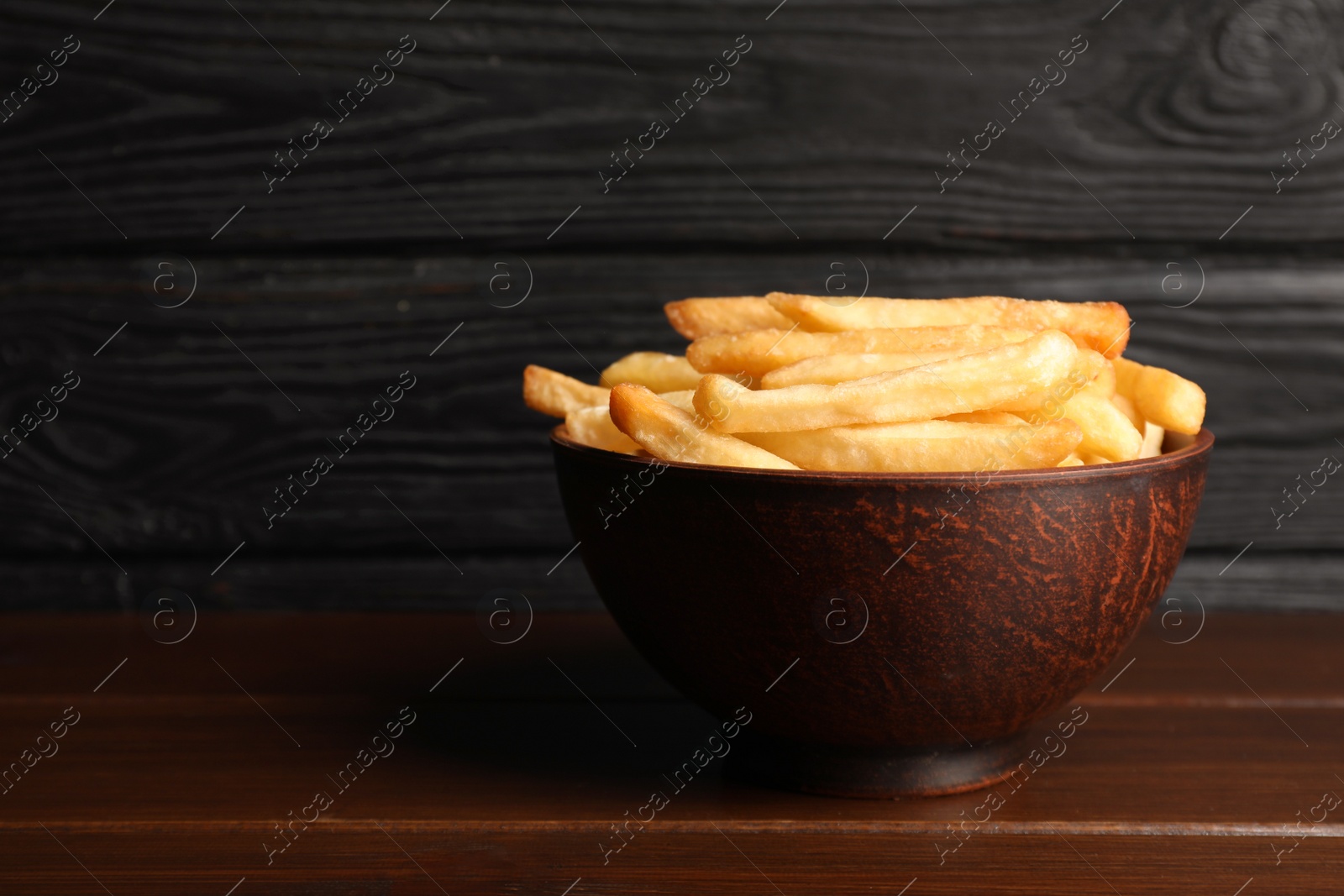 Photo of Delicious fresh french fries in bowl on wooden table, space for text